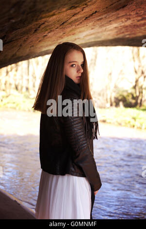 Beautiful teenage girl looking over her shoulder whilst standing under a bridge with a river in the background Stock Photo