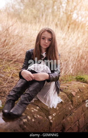 Beautiful teenage girl sitting on a stone wall looking looking straight to camera Stock Photo