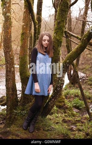 Pretty teenage girl leaning against a tree with a river in the background Stock Photo