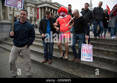 Stag party humiliation pranks as the groom is dressed up as a woman in an orange dress and wig then pushed into the fountains in Trafalgar Square in London, England, United Kingdom. There is a strong tradition at the British Stag Do, to play tricks on the stag at least once. In this case, he had no idea where he was headed, and so blindfolded was perched on the waters edge and thrown in. The stag seemed not to mind but was also, somewhat the worse for wear. Stock Photo