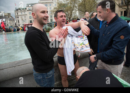 Stag party humiliation pranks as the groom is dressed up as a woman in an orange dress and wig then pushed into the fountains in Trafalgar Square in London, England, United Kingdom. There is a strong tradition at the British Stag Do, to play tricks on the stag at least once. In this case, he had no idea where he was headed, and so blindfolded was perched on the waters edge and thrown in. The stag seemed not to mind but was also, somewhat the worse for wear. Stock Photo