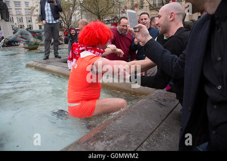 Stag party humiliation pranks as the groom is dressed up as a woman in an orange dress and wig then pushed into the fountains in Trafalgar Square in London, England, United Kingdom. There is a strong tradition at the British Stag Do, to play tricks on the stag at least once. In this case, he had no idea where he was headed, and so blindfolded was perched on the waters edge and thrown in. The stag seemed not to mind but was also, somewhat the worse for wear. Stock Photo