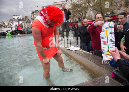 Stag party humiliation pranks as the groom is dressed up as a woman in an orange dress and wig then pushed into the fountains in Trafalgar Square in London, England, United Kingdom. There is a strong tradition at the British Stag Do, to play tricks on the stag at least once. In this case, he had no idea where he was headed, and so blindfolded was perched on the waters edge and thrown in. The stag seemed not to mind but was also, somewhat the worse for wear. Stock Photo