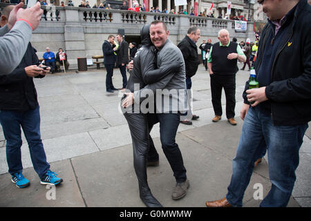 Stag party humiliation pranks as the groom is dressed up in a gimp costume and pushed into the fountains in Trafalgar Square in London, England, United Kingdom. There is a strong tradition at the British Stag Do, to play tricks on the stag at least once. In this case, he had no idea where he was headed, and so blindfolded was perched on the waters edge and thrown in. The stag seemed not to mind but was also, somewhat the worse for wear. Stock Photo