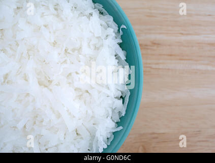 Top close view of a portion of sweetened coconut flakes in a small bowl atop a wood table top. Stock Photo