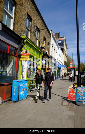 young Caucasian couple holding hands whilst walking pass shops on Penton Street, London Stock Photo