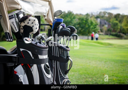 Golf clubs on back of golf cart with golfers in background Stock Photo