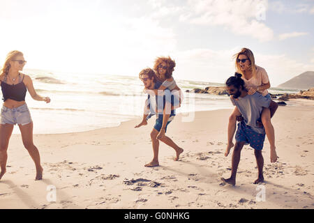 Group of friends having fun on the beach vacation, men piggybacking women.
