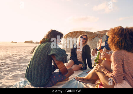 Portrait of young man playing guitar for friends. Group of friends having fun at the beach party. Young men and women sitting on