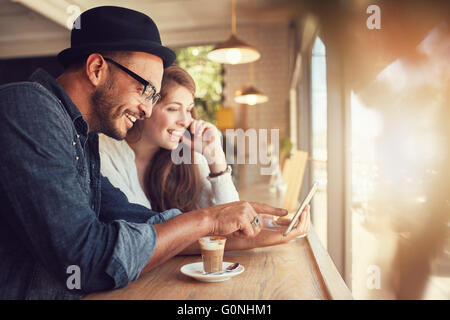 Smiling young couple in a coffee shop using touch screen computer. Young man and woman in a restaurant looking at digital tablet