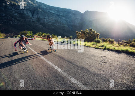 Young couple skating down on the road. Young man and woman having fun while skating together on a sunny day. Stock Photo