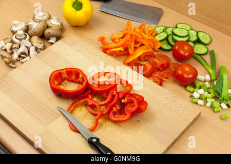 Cutting knife laying on top of a freshly ring cut red bell pepper on a chopping board aside some mixed vegetables Stock Photo