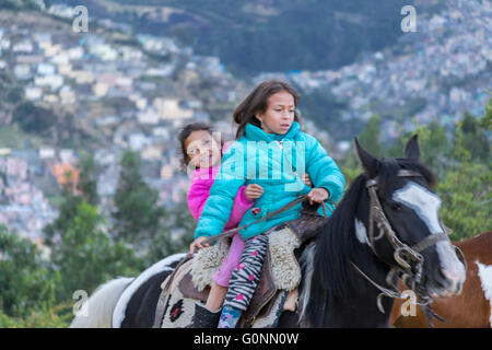 QUITO, ECUADOR, OCTOBER - 2015 - Two indigenous ecuadorian girls riding a horse at panecillo hill in Quito, Ecuador Stock Photo