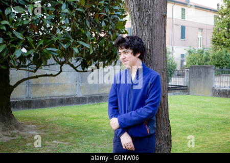 young boy smiles leaning against the trunk of a catalpa tree in garden Stock Photo