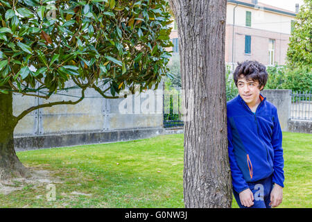 young boy smiles leaning against the trunk of a catalpa tree in garden Stock Photo