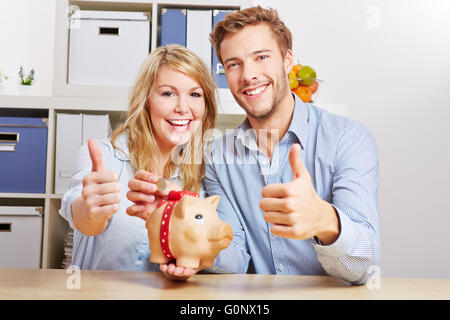 Smiling happy couple with piggy bank and monay holding their thumbs up Stock Photo