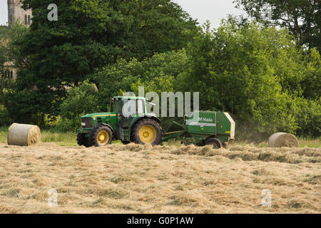 Silage or hay making - man is driving green farm tractor pulling a round baler, working in a field - Great Ouseburn, North Yorkshire, England, UK. Stock Photo