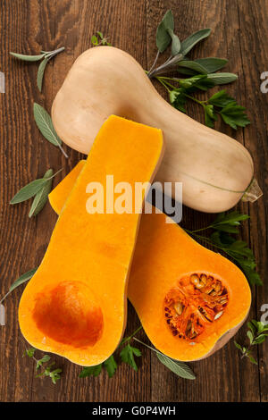 Fresh butternut squash whole and cut with sage and parsley on brown wooden background, from above Stock Photo