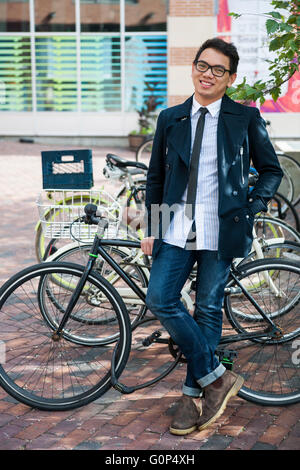 Young smiling asian business man or student standing in front of bicycle parking rack on city street Stock Photo