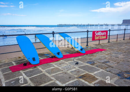 Sign for Saltburn Surf School on the promenade railings with surf boards Stock Photo