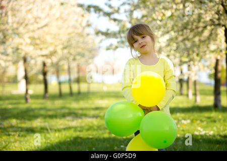 Cute little girl playing with balloons in a blooming apple tree garden, spring sunny late afternoon Stock Photo