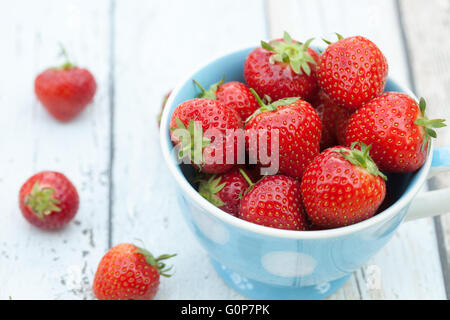 Fresh strawberries in a blue and white spotted mug. Small group of strawberries on the table beside the mug. Stock Photo