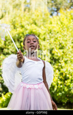 Cute mixed-race girl wearing a fairy dress and pointing the camera with her magic wand Stock Photo