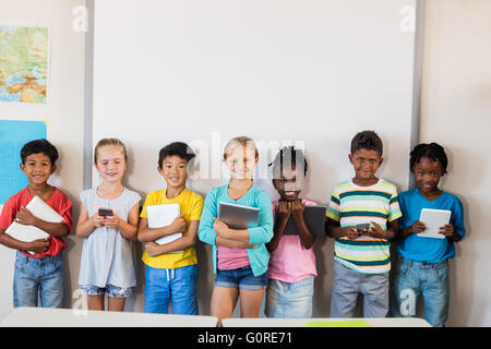 Smiling pupils standing with technology Stock Photo