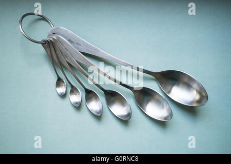 A set of brushed stainless steel measuring spoons on a green background Stock Photo