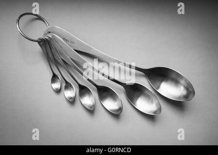 A set of brushed stainless steel measuring spoons on a plain background Stock Photo