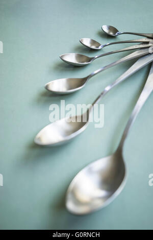 A set of brushed stainless steel measuring spoons on a green background Stock Photo