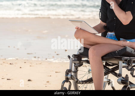 Young woman in wheelchair using  tablet at the beach Stock Photo