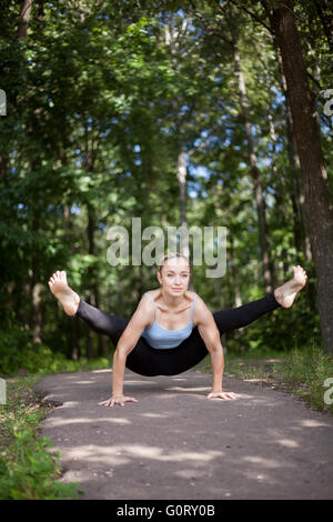 Beautiful sporty fit yogi girl working out in forest, practicing yoga outdoors on summer day, doing arm balance, handstand Stock Photo