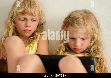 two girl sitting and playing with digital device Stock Photo