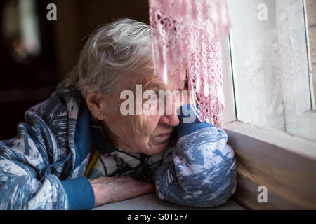 An elderly woman sadly looking out the window. Stock Photo