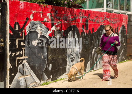 A woman walks her dog past the Subcomandante Marcos and Benazir Bhutto Rise All Freedom Fighters street mural on a wall in the trendy Wicker Park neighborhood in the West Town community in Chicago, Illinois, USA Stock Photo