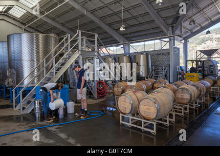 Workers topping up wine barrel in fermentation area at Mending Wall Winery along Silverado Trail in Napa Valley California Stock Photo