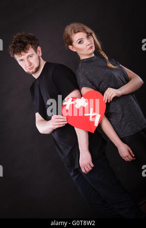 Broken heart difficult love concept. Sad unhappy couple woman and man holding paper red heart fixed with plaster bandage. Rift in relations. Stock Photo