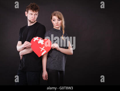 Broken heart difficult love concept. Sad unhappy couple woman and man holding paper red heart fixed with plaster bandage. Rift in relations. Stock Photo