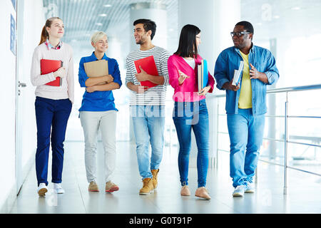 Group of college learners with books walking down corridor and talking Stock Photo