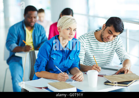 Multi-ethnic college students sitting by desk and writing lecture Stock Photo