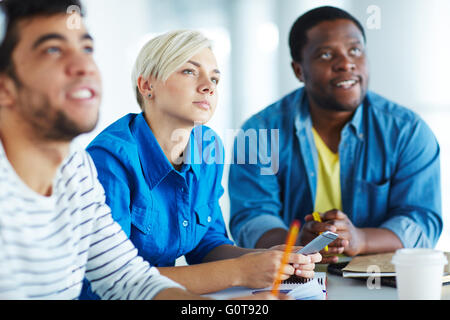 Serious student listening to lecturer among her group-mates Stock Photo