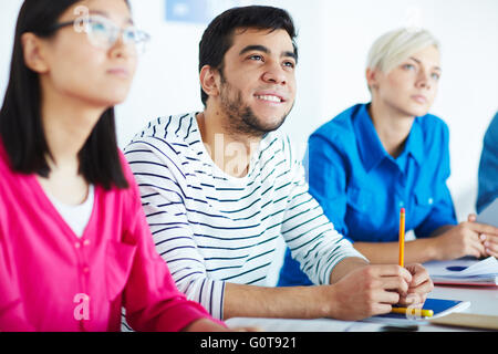 Students at seminarHappy Latino guy listening to lecture among college friends Stock Photo