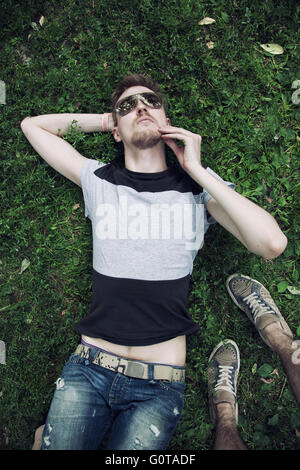 Young men wearing a sunglasses lying on the grass in park Stock Photo