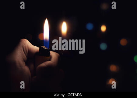Male hand holding a burning lighter in the dark Stock Photo