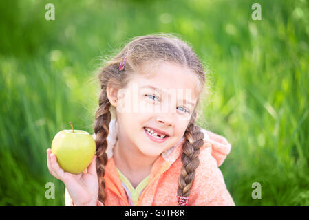 Sweet girl with a fallen toth holding an apple in her hand on nature Stock Photo