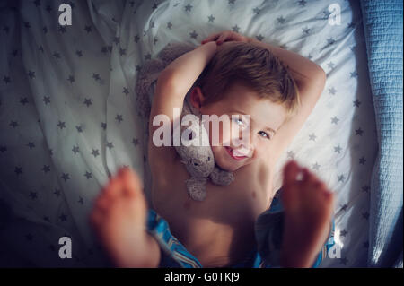 Smiling Boy lying on bed with cuddly toy Stock Photo