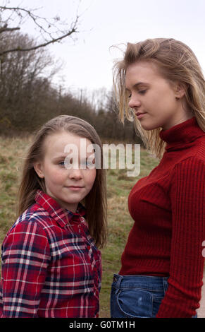 Two young girls smile at each other as they lie front down on a bed ...