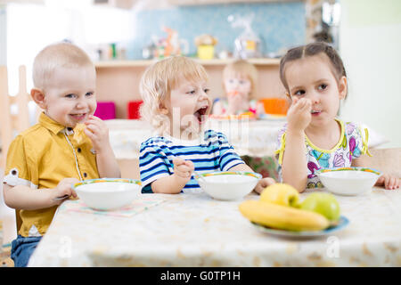Funny little kid with open mouth eating in kindergarten group Stock Photo