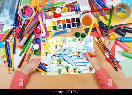 airliner fly high above the earth, child drawing, top view hands with pencil painting picture on paper, artwork workplace Stock Photo